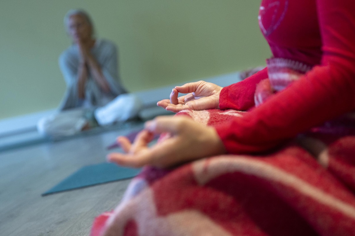 En elev sitter i meditasjon med læreren i bakgrunnen